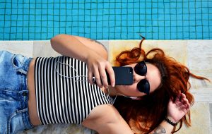 woman at pool with earbuds looking at phone